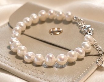 May include: A white pearl bracelet featuring a silver-toned metal chain extension and a lobster clasp. The bracelet rests on a light beige square pouch with a gold-toned snap button and the embossed text STONE & SONDER on the front surface.