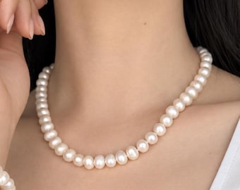 May include: A single-strand necklace composed of uniform, round, off-white pearls. The pearls are strung together in a continuous line, resting against the neck. A small portion of a matching pearl bracelet with a gold-toned chain is visible.