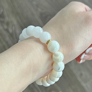 May include: A white beaded bracelet with a gold accent. The beads are round and have a smooth, polished finish.