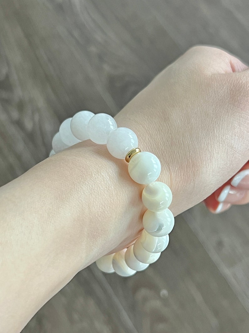 May include: A white beaded bracelet with a gold accent. The beads are round and have a smooth, polished finish.