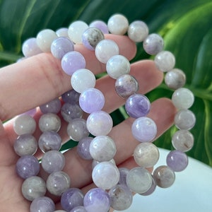Puede incluir: Tres pulseras de amatista con cuentas redondas en tonos de morado y blanco.
