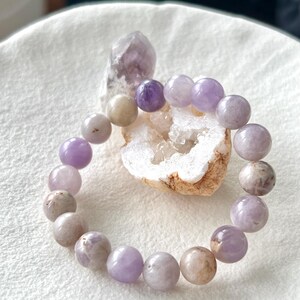 Puede incluir: Un brazalete de amatista p&uacute;rpura con cuentas redondas. El brazalete est&aacute; hecho de piedras naturales y tiene un color p&uacute;rpura claro.