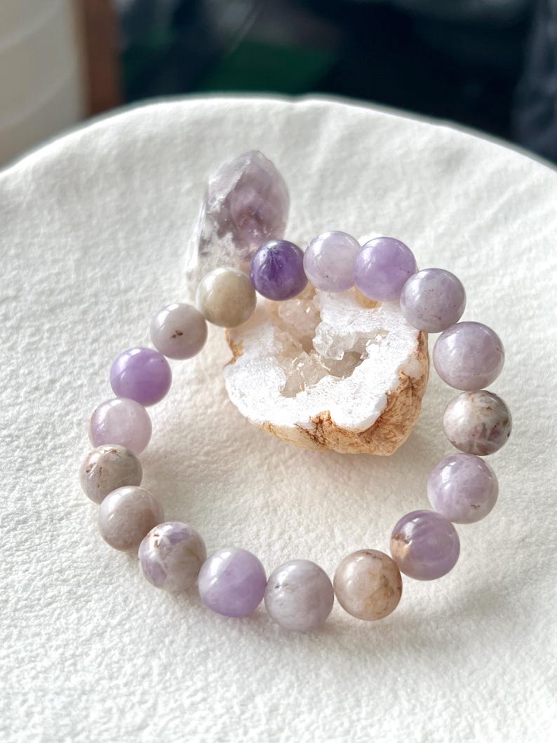 Puede incluir: Un brazalete de amatista p&uacute;rpura con cuentas redondas. El brazalete est&aacute; hecho de piedras naturales y tiene un color p&uacute;rpura claro.
