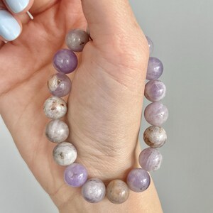 Puede incluir: Un brazalete de piedras preciosas de color p&uacute;rpura y blanco con cuentas redondas.