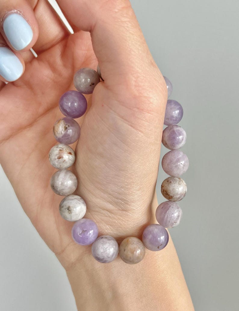 Puede incluir: Un brazalete de piedras preciosas de color p&uacute;rpura y blanco con cuentas redondas.