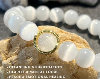 May include: White gemstone bracelet with a gold accent. The bracelet is on a light brown rock. The text on the image reads: "Cleansing & Purification, Clarity & Mental Focus, Peace & Emotional Healing."