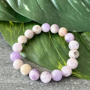 Puede incluir: Un brazalete de piedras preciosas de color p&uacute;rpura y blanco con cuentas redondas. El brazalete est&aacute; hecho de piedras naturales y es un hermoso accesorio para cualquier ocasi&oacute;n.