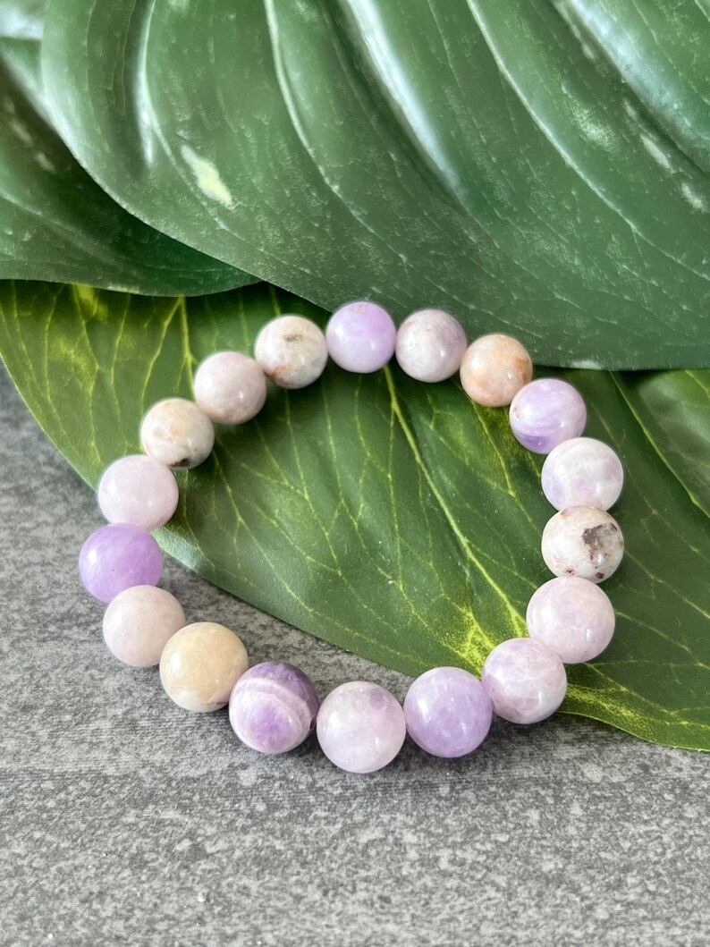 Puede incluir: Un brazalete de piedras preciosas de color p&uacute;rpura y blanco con cuentas redondas. El brazalete est&aacute; hecho de piedras naturales y es un hermoso accesorio para cualquier ocasi&oacute;n.