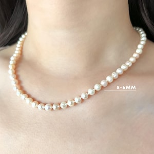 K&ouml;nnte beinhalten: Eine einreihige Halskette aus runden, cremewei&szlig;en Perlen. Die Perlen haben einen Durchmesser von 5-6 mm. Die Kette wird in einer L&auml;nge von 16 Zoll gezeigt. Der Text 5-6MM ist neben den Perlen sichtbar, sowie der Text Model wears 16 inches.