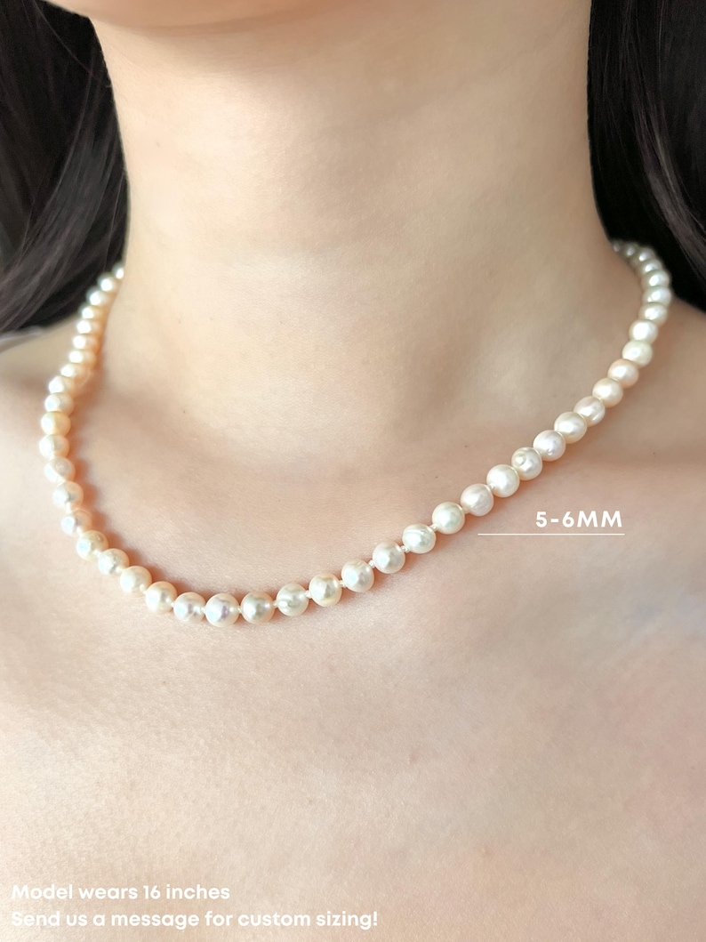 K&ouml;nnte beinhalten: Eine einreihige Halskette aus runden, cremewei&szlig;en Perlen. Die Perlen haben einen Durchmesser von 5-6 mm. Die Kette wird in einer L&auml;nge von 16 Zoll gezeigt. Der Text 5-6MM ist neben den Perlen sichtbar, sowie der Text Model wears 16 inches.