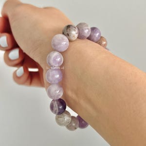 Puede incluir: Un brazalete de amatista p&uacute;rpura con cuentas de 10 mm. El brazalete se muestra en la mu&ntilde;eca de una persona. Tama&ntilde;o de mu&ntilde;eca del modelo: 5,5 pulgadas (XS)