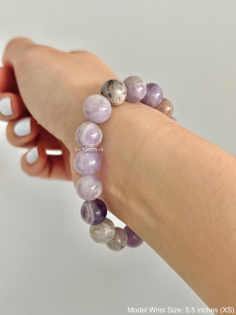 Puede incluir: Un brazalete de amatista p&uacute;rpura con cuentas de 10 mm. El brazalete se muestra en la mu&ntilde;eca de una persona. Tama&ntilde;o de mu&ntilde;eca del modelo: 5,5 pulgadas (XS)