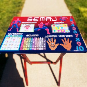 May include: A blue and red learning table with a Spiderman theme. The table features an alphabet, colors, shapes, numbers, and body parts. The table is made of wood and has a metal frame.