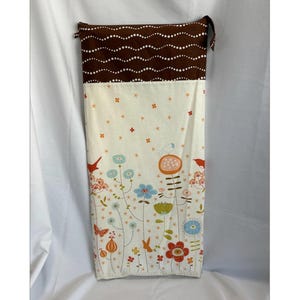 May include: A long, rectangular fabric bag with a brown polka-dot top and a floral design on the bottom. The floral design features birds, butterflies, and various flowers in shades of red, blue, orange, and green on a cream background.