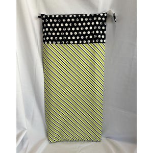 May include: A tall, rectangular fabric bag with a black and white polka dot top and a green and black striped bottom. The bag has a drawstring closure at the top and is likely used for storage or carrying items.