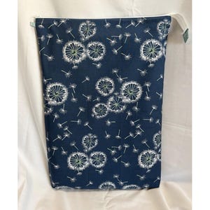 May include: A navy blue zippered bag with a white dandelion pattern. The dandelions have white seed heads and green centers. The bag has a white zipper and a small green tab on the side.