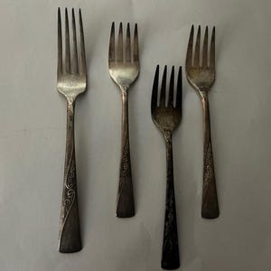 May include: Four silver forks with ornate designs on the handles.