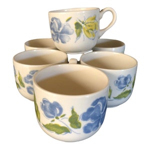 May include: Set of six white ceramic mugs with blue and green floral designs. The mugs have a rounded shape and a simple handle.