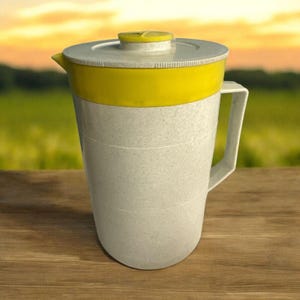 Puede incluir: Una jarra de plástico blanca y amarilla de estilo vintage con tapa. La jarra tiene un asa y un pico vertedor para facilitar el vertido. El diseño incluye una banda amarilla alrededor de la parte superior y una tapa amarilla con un pequeño pomo. La jarra está sobre una superficie de madera.