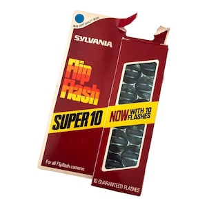 May include: A red and yellow box of Sylvania Flip Flash Super 10 camera flash bulbs. The box says "NOW WITH 10 FLASHES" and "10 GUARANTEED FLASHES".