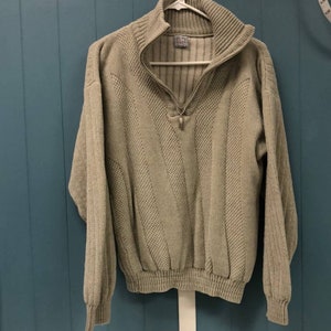 May include: A beige knitted sweater with a zippered collar and a ribbed texture. The sweater has a vertical striped pattern.