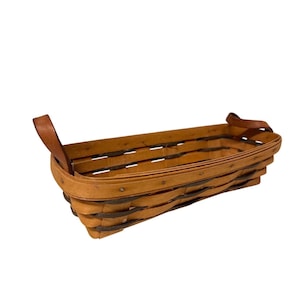 May include: A rectangular, woven basket with a light brown finish and dark brown accents. The basket features two brown leather handles and is made of wooden slats. The basket is empty and sits on a white background.
