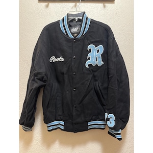 May include: Black Roots varsity jacket with light blue and white striped accents on the collar, cuffs, and hem. Features a large light blue letter "R" patch and the number "'13" on the sleeve. The Roots logo is embroidered on the chest.
