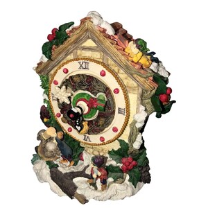May include: A decorative cuckoo clock with a festive Christmas theme. The clock features a cream-colored face with Roman numerals and a wreath design. The clock is adorned with holly, berries, and figurines of children and animals.