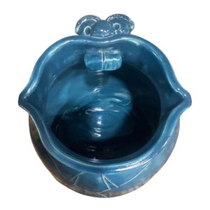 Puede incluir: Jarra de cerámica de color turquesa con un diseño único. La jarra presenta una parte superior ancha y abierta con un pico y un asa decorativa. El exterior tiene una superficie texturizada con patrones geométricos grabados cerca de la base.