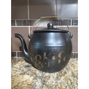 Può includere: Teiera in ceramica nera con coperchio e beccuccio curvo. La teiera ha un manico color oro e le parole "Cookie Jar" sono scritte sul lato in oro.