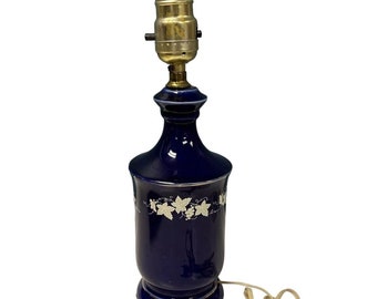 May include: A cobalt blue ceramic table lamp with a white floral design. The lamp has a gold-tone base and a white cord.