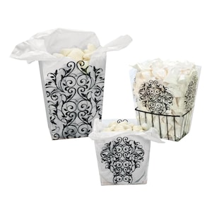 May include: Three decorative containers filled with white items. The containers include a tall, paper-lined box with a black and white scroll design, a wire basket, and a smaller box, all with similar designs.