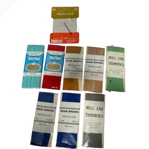Könnte beinhalten: Eine Sammlung von Vintage-Nähzubehör, darunter Gummikordel, Schrägband, Nahtband und Mühlenendbesätze. Die Artikel sind in verschiedenen Farben wie Blau, Rot, Grün und Beige erhältlich. Die Verpackung enthält Text und Branding.