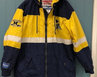 May include: A blue and yellow hooded jacket with the University of Michigan logo and the Big Ten Conference logo. The jacket has a zipper closure and two pockets.