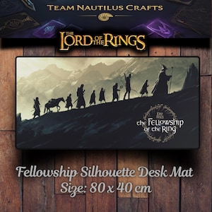Könnte beinhalten: Schreibtischunterlage mit einer Silhouette von Charakteren aus Der Herr der Ringe, vor einer Bergkulisse. Die Matte trägt die Aufschrift "Fellowship Silhouette Desk Mat" und "Size: 80 x 40 cm". Der Hintergrund hat einen Farbverlauf von hellen und dunklen Farben.