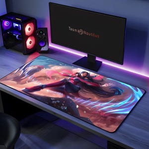 May include: A rectangular desk mat featuring a vibrant digital illustration of a long-haired character in a dynamic pose with flowing pink ribbons and glowing blue energy effects. The mat has a black border and rests on a desk surface.