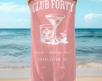 May include: A pink beach towel with the words "CLUB FORTY" at the top. Below are illustrations of a cocktail and a rocks glass. The text "Emily's Birthday Bash, Charleston, SC, EST 1985" is also printed on the towel.