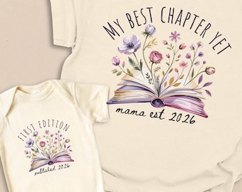 May include: A cream-colored t-shirt and a matching baby bodysuit, both featuring a graphic of an open book with colorful flowers emerging from the pages. The t-shirt reads MY BEST CHAPTER YET mama est 2026, and the bodysuit reads FIRST EDITION published 2026.