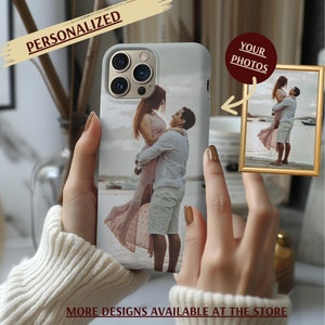 May include: A white phone case with a photo of a couple embracing on a beach. The case has a cutout for the camera lens and a raised lip around the edges to protect the screen. The text "YOUR PHOTOS" is visible in the upper right corner of the image.
