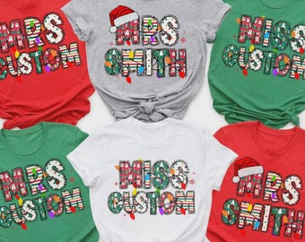 May include: A collection of short-sleeved t-shirts in red, gray, green, and white. Each shirt features a festive design with the words "MRS CUSTOM" or "MISS CUSTOM" in a colorful, Christmas-themed font, with a Santa hat on some.