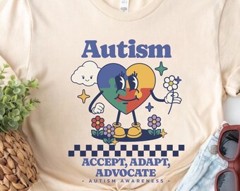 May include: A beige t-shirt with a colorful heart design and the text "Autism Accept, Adapt, Advocate - Autism Awareness".