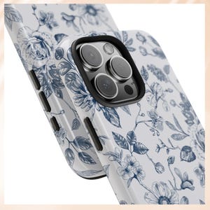 May include: A white phone case with a blue floral pattern. The case has a raised camera bump with three black camera lenses.