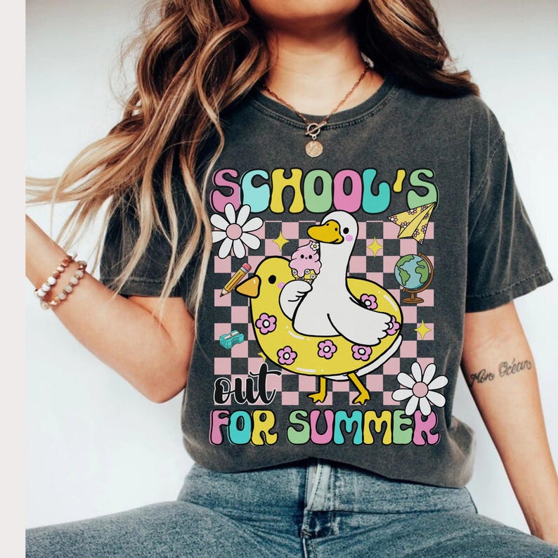 Pu&ograve; includere: T-shirt grigio scuro con una grafica colorata che recita "SCHOOL'S OUT FOR SUMMER". Il design presenta un'anatra bianca su un anello gonfiabile giallo, un mappamondo e fiori. La maglietta ha uno stile vintage e retr&ograve;.