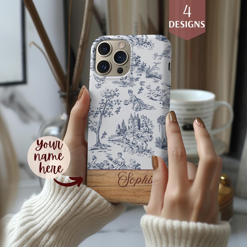 May include: A white phone case with a blue and white toile pattern. The case has a wood-look bottom with the name "Sophie" engraved on it.