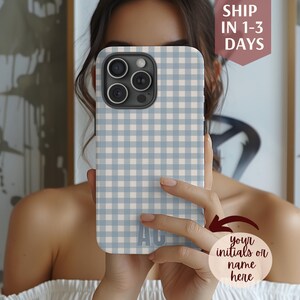 May include: A light blue and white gingham patterned phone case with the initials "AG" on the bottom. The phone case is held up in front of a person. The text "Ship in 1-3 days" is visible.