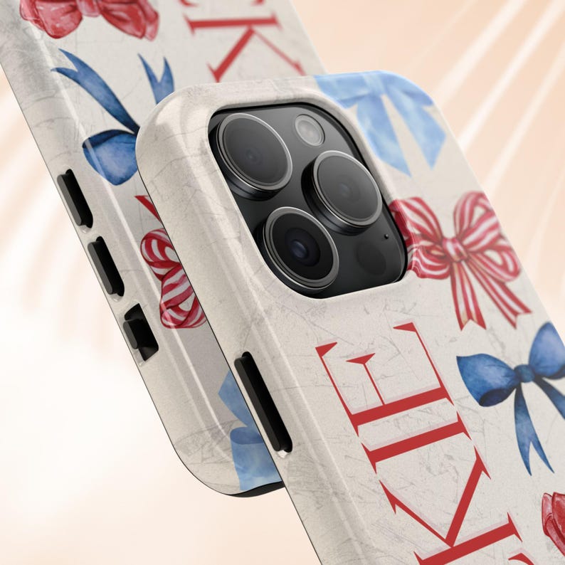 Puede incluir: Una funda de tel&eacute;fono blanca con un patr&oacute;n de lazos rojos y azules y las letras "KIE" en rojo. La funda tiene una textura similar al m&aacute;rmol y un recorte para la c&aacute;mara.