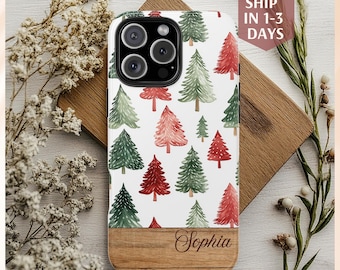 Puede incluir: Funda de iPhone blanca con un estampado de árboles de Navidad verdes y rojos en acuarela. La parte inferior de la funda tiene un diseño de vetas de madera con el nombre "Sophia" grabado. Rodeada de flores secas y vegetación.