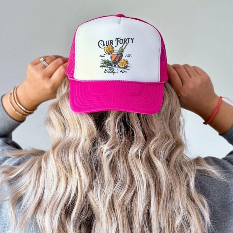 Puede incluir: Gorra de camionero rosa con una malla blanca en la parte posterior. La parte delantera de la gorra presenta un gr&aacute;fico de un c&oacute;ctel con el texto "Club Forty est 1985 Emily's 40s".