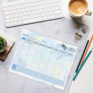May include: A weekly schedule notepad with a watercolor design in blue and yellow. The notepad has a header that says "My Weekly Schedule" and includes sections for each day of the week, with space for notes. A white keyboard, pencils, and a cup of coffee are also visible.