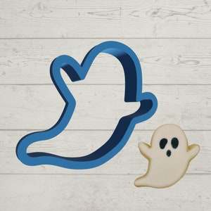 May include: Blue plastic cookie cutter shaped like a ghost, with a white ghost cookie next to it.